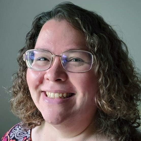 A smiling white woman with glasses and curly brown hair.